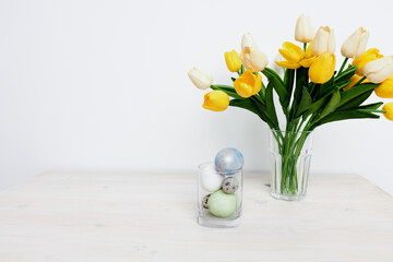 a bouquet of tulips on the table and Easter eggs in a glass