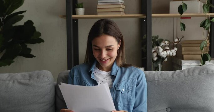 Attractive woman sit on sofa hold in hands sheets read great news in letter feels happy celebrate success. University admission, scholarship got, career growth and advance, bank loan approved concept
