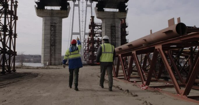 Male workers walking and discussing bridge construction