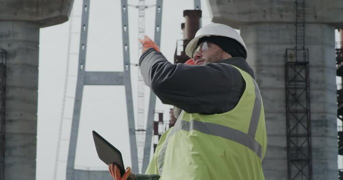 Male engineers discussing bridge drafts on tablet