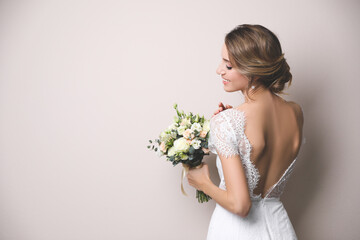 Young bride with elegant hairstyle holding wedding bouquet on beige background. Space for text - Powered by Adobe