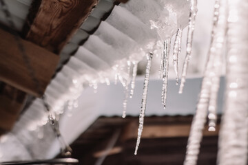 Spring icicles hang on the roof of the house. End of winter.