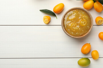Delicious kumquat jam in bowl and fresh fruits on white wooden table, flat lay. Space for text
