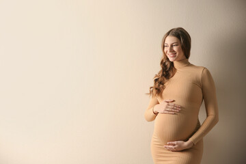 Happy pregnant woman touching her belly on beige background. Space for text