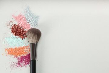Makeup brush and scattered eye shadows on light grey background, flat lay. Space for text