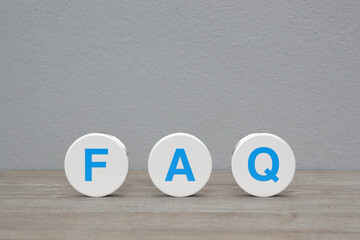 FAQ letter on white circle shape on wooden table over white wall background, Frequently asked...