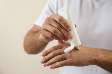 Man applying cream from tube onto hand on beige background, closeup