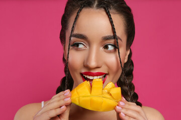 Young woman eating fresh mango on pink background. Exotic fruit