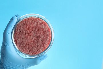 Obraz na płótnie Canvas Scientist holding Petri dish with minced lab grown meat on light blue background, closeup. Space for text