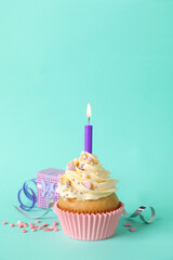 Birthday cupcake with burning candle, gift box  and sprinkles on turquoise background