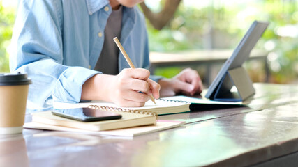 Fototapeta premium Online studying class, Student man hand writing on notebook while using digital tablet for e learning, Adult male university, college student study online course at home, education, Work from home