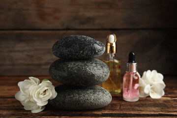 Stack of grey spa stones, flowers and oils on wooden table