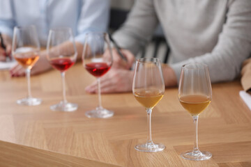 Different sorts of wine in glasses prepared for tasting and sommeliers at wooden table indoors, closeup