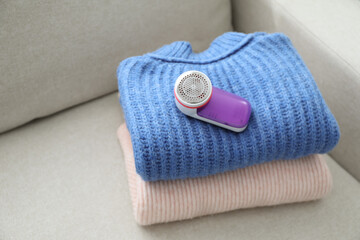 Modern fabric shaver and woolen sweaters on sofa indoors