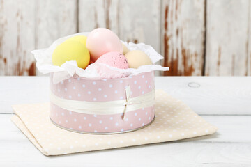 Pink dotted can with Easter eggs on wooden table.