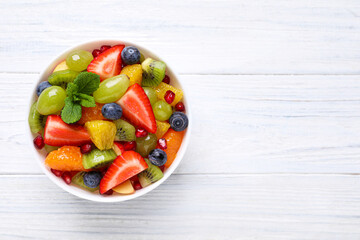 Delicious fresh fruit salad in bowl on white wooden table, top view. Space for text