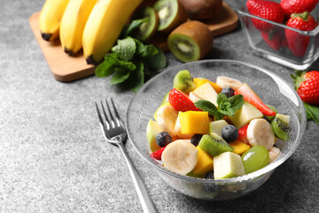 Delicious fresh fruit salad in bowl on grey table, space for text
