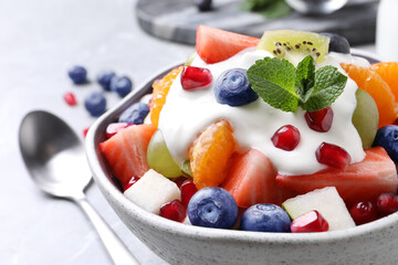 Delicious fruit salad with yogurt in bowl on table, closeup