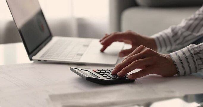 Woman working using calculator and laptop, close up female hands calculates costs, manage finances, makes payments through secure bank system, analyze company charges prepare financial report concept