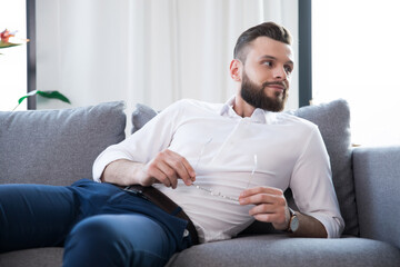 Close up photo of confident stylish handsome bearded business man in glasses and formal smart wear while he is sitting on the couch