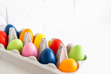 Stylish easter eggs in carton tray on white wooden background, top view. Modern colorful easter eggs painted with natural dye in different colors. Happy Easter, eco concept. Space for text