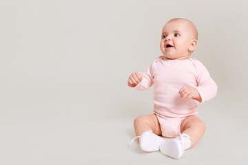 Happy excited infant child baby girl toddler wearing bodysuit and socks sitting on floor isolated...