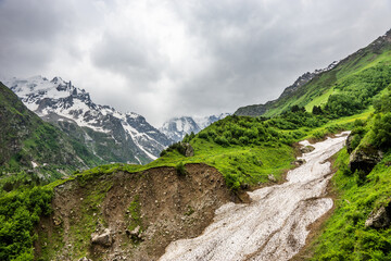 Avalanche path in the alpine meadow in cloudy summer day. Caucasus mountains near Elbrus, Russia.