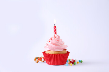Delicious birthday cupcake with burning candle, sprinkles and streamer on white background