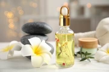 Beautiful spa composition with essential oil and plumeria flowers on white table against blurred lights