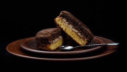 A tiramisu cake with a silver spoon on a clay plate. Side view.