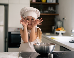 Small cute girl in special clothes and  funny chef cap with pompom. Making cookie at home on kitchen, make fun enjoy together. Child make dessert