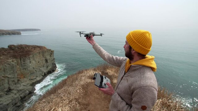 A man is landing the copter on his hand standing on the picturesque cliff edge. Filming beautiful marine landscape