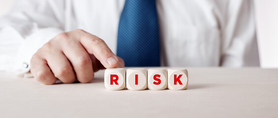 Businessman pressing his finger on the wooden cubes with the word risk. Risk taking, risk management or assessment