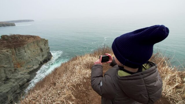 4 years old boy is taking photo of marine landscape standing on the high cliff edge