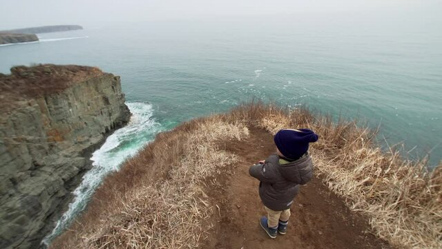 4 years old boy is taking photo of beautiful marine landscape standing on the high cliff edge