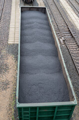 A green metal freight train car with a pile of coal evenly piled to the top, standing on rails among empty railway tracks, the gaps between which are lined with concrete tiles, a view from above.