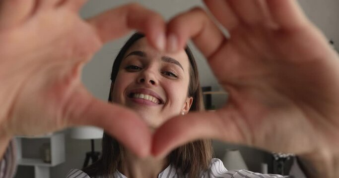 Beautiful young woman feels happy sharing love join fingers showing heart shape at camera, close up. Symbol of charity, health care and cardiac checkup, voluntary social work, organ donation concept