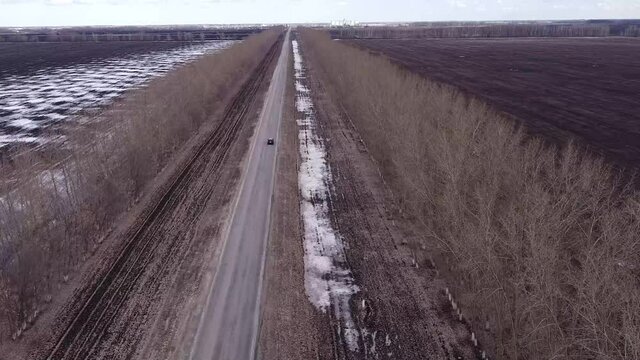 Black car rides on a field road in spring drone