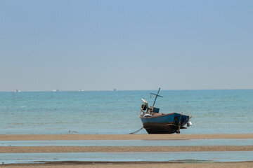Obraz premium fisherman's fishing boat on sand at a fishing village beach There is an island and sea background with the daytime sky. stranded fishing boat After the sea has receded