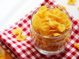 raw farfalle pasta in a bowl, italian pasta - farfalle in a glass bowl on a white background. Various types of Italian durum wheat pasta for Mediterranean cuisine. Top view, place for text. Banner. 