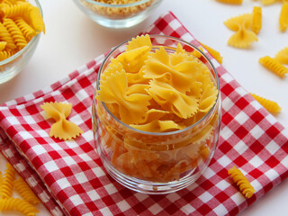 raw farfalle pasta in a bowl, italian pasta - farfalle in a glass bowl on a white background. Various types of Italian durum wheat pasta for Mediterranean cuisine. Top view, place for text. Banner.