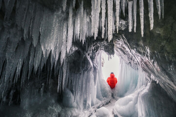 Little figure of woman traveler in  frozen winter cave in the rock. Baikal grottoes