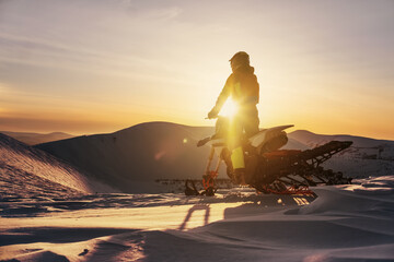 Fototapeta na wymiar Snowbike rider standing on top of mountain during sunset with atmospheric landscape view