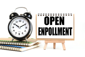 Open enrollment. text on white notepad paper on a stand next to our desk clock on a sideboard. on white background