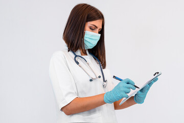 Young brunette doctor writing records after visit. She is wearing white uniform and protective...