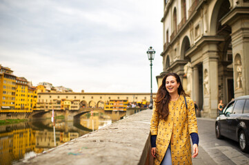 A tourist girl with an orange coat happily walks on the embankment in Florence, Italy