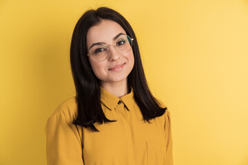 Obraz premium Cute, knife brunette with glasses posing against the background of an orange wall. Isolated on an empty wall, close up