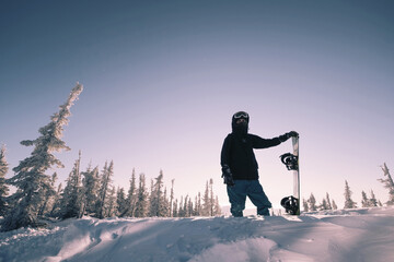 Silhouette of a snowboarder standing with  board on the snow. Winter sunny day close to sunset