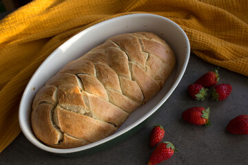 Freshly baked challah bread in oval ceramic baking form, yellow fabric towel and juicy strawberries...