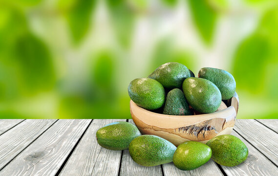 fresh avocado fruit standing in wooden round bowl, on wooden background, front view, in front of blurred background
